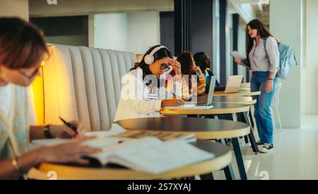 College students concentrating on their studies in a contemporary library setting, working collaboratively with laptops and notes, fostering an atmosp Stock Photo