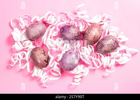 Painted eggs for Easter in white decorative nest on pink surface. Easter flat lay with copy space Stock Photo