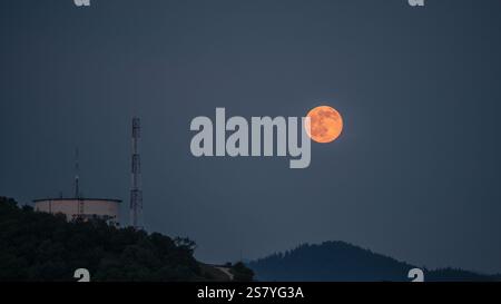 A striking image of a super moon rising above a hilltop water tank and communication tower, set against a tranquil twilight sky. The glowing moon adds Stock Photo
