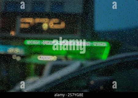 a rainy urban evening through a glass window, with sharp raindrops in the foreground and a blurred background featuring vibrant neon lights in shades Stock Photo