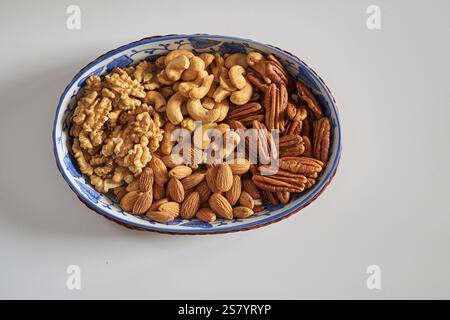 Assorted nuts in a stoneware container with a straw basket, on a white background. Almonds, Walnuts, Cashews and Chestnuts Stock Photo