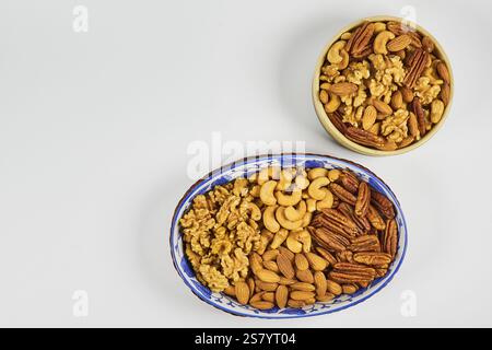 Assorted nuts in a stoneware container with a straw basket, on a white background. Almonds, Walnuts, Cashews and Chestnuts Stock Photo