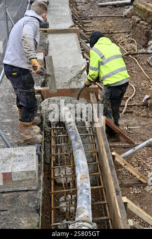 Concrete being pumped into timber formwork with steel reinforcing, two men levelling and compacting with vibrating machine Stock Photo