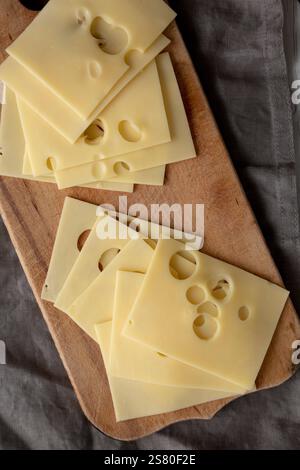 Slices of Maasdam cheese on a wooden board, top view. Close-up. Stock Photo