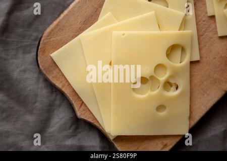 Slices of Maasdam cheese on a wooden board, top view. Close-up. Stock Photo