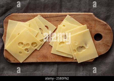 Slices of Maasdam cheese on a wooden board, top view. Close-up. Stock Photo