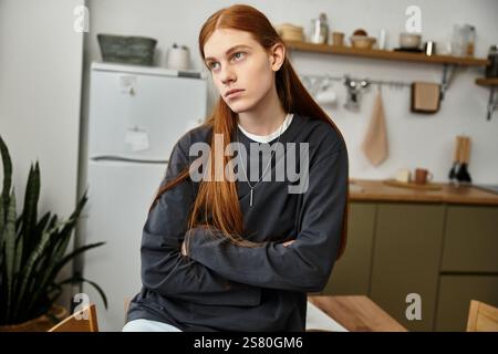 Casual young man sits thoughtfully in his stylish apartment, showcasing a relaxed vibe. Stock Photo