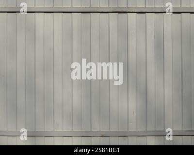 gray metal fence in soft sunlight with pale shadow spots, with vertical raised stripes and horizontal crossbars in the structure, graphic texture Stock Photo