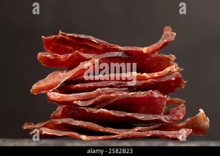 dried pieces of pork, dried dried meat from meat tenderloin with spices and salt on black slate Stock Photo