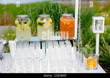 Glass jars with lemonade and orange juice, empty glasses and orange slices on a table at a garden party Stock Photo