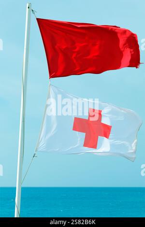 Life guard (cruz roja) flags flying at Piedra Playa beach, El Cotillo, Fuerteventura. Taken December 2024. Stock Photo
