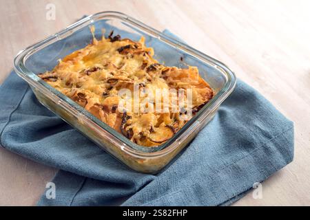Baked casserole with chicory, apple, onion and bacon gratinated with cheese in an ovenproof glass dish on a blue kitchen towel, copy space, selected f Stock Photo