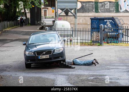 Man underneath a car, using a jack to lift it up, while he works on the undercarriage in Turku, Finland Stock Photo