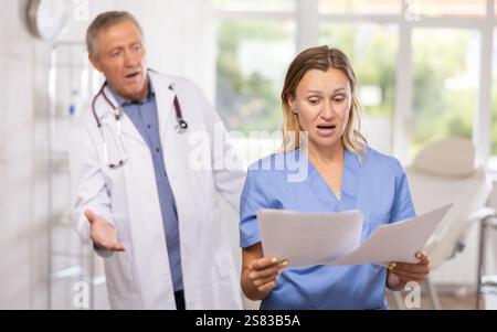 Upset female doctor with papers stading in office with disgruntled chief Stock Photo
