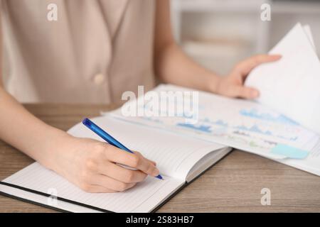Young woman writing down something while working with documents in office. Closeup Stock Photo