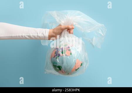 Female hand with model of earth in plastic bag on blue background. Microplastic Awareness Month Stock Photo