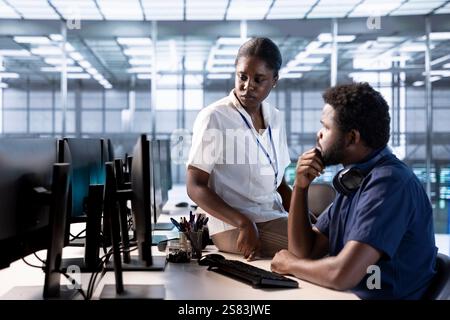 Supervisor checking on data center employee creating technical documentation for software applications. Manager supervising IT expert working in server room maintaining databases Stock Photo