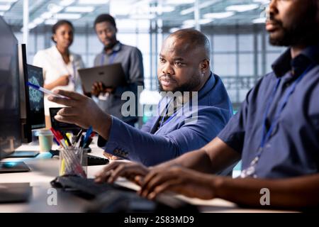 Teamworking engineers in data center using diagnostic tools and system monitoring software to identify root cause of errors. Coworkers doing brainstorming in server farm, mending equipment together Stock Photo