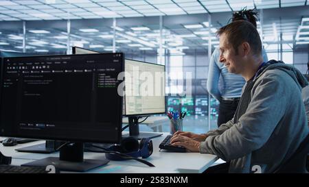IT technician looking at PC screen, working in network security data center, ensuring optimal performance. Man supervising server hub, monitoring energy consumption across rigs, camera B Stock Photo