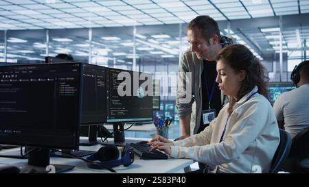 Woman requesting help from senior engineer to fix error in high tech AI data center. Employee in need of aid from IT professional to repair artificial intelligence supercomputers, camera B Stock Photo