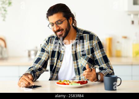 Handsome indian man using cellphone while having breakfast Stock Photo