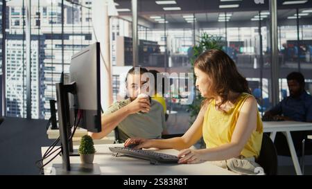 Man with paraplegia drinking coffee, checking progress done by employee doing code review to fix bugs. Worker code, being supervised by manager in wheelchair enjoying beverage, camera B Stock Photo