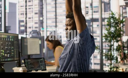 System administrator in pain, suffering muscle sprain while developing machine learning APIs. Man feeling backache from sitting at desk all day while training predictive models Stock Photo