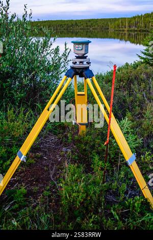 A yellow tripod is set up in a field next to a body of water. The tripod is being used to take measurements of the area Stock Photo