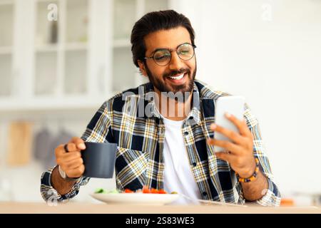 Smiling idian man eating healthy food and using phone Stock Photo