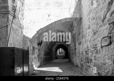 A narrow, dark tunnel with a black door at the end. The tunnel is empty and the light is shining on the wall Stock Photo