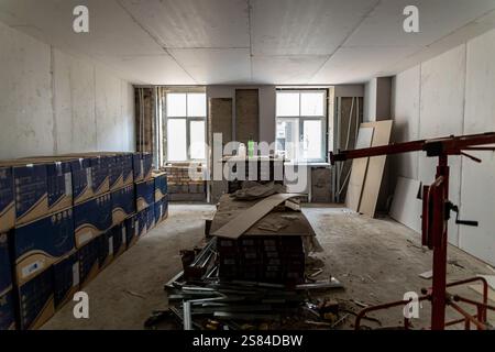 Room with unfinished walls, exposed brick, Cersanit boxes, tools on a table, a red construction lift, and natural light from two windows. Stock Photo