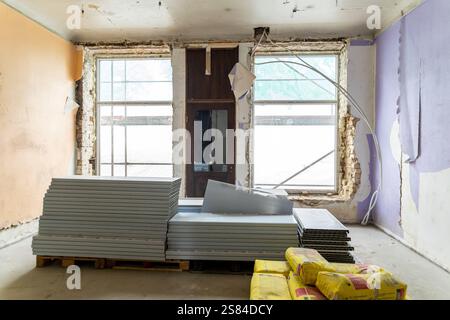 Interior space under renovation featuring exposed brick, drywall on a pallet, yellow construction bags, peeling paint, and hanging electrical wires. Stock Photo
