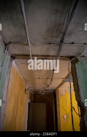 An unfinished interior space with exposed wiring, faded yellow and green walls, visible cracks, and a partially open door in the background. Stock Photo