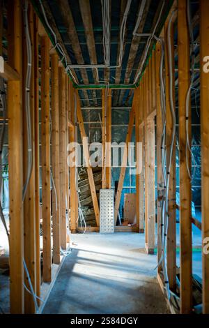 Exposed wooden framing, visible wiring, and unfinished concrete floor in a building under construction. Insulation and structural elements are visible Stock Photo