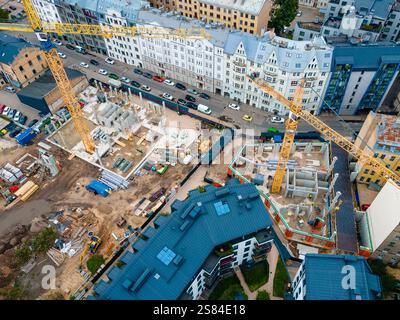 Active construction site with two yellow tower cranes, surrounded by multi story buildings with gabled roofs and mixed architectural styles. Stock Photo