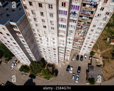 Cluster of tall, rectangular apartment buildings with balconies, parking area, paved roads, and patches of vegetation, seen from above. Stock Photo