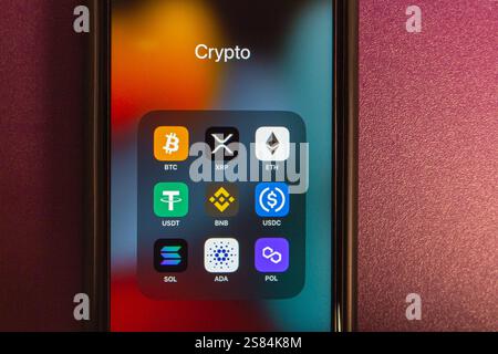BTC, XRP, ETH, USDT, BNB, USDC, SOL, ADA and POL icons are displayed on an iPhone, with copy space on background. Popular crypto concept image. Stock Photo