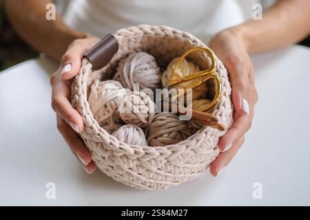 Female hands holding a crocheted basket with skeins of cotton yarn in natural tones Stock Photo