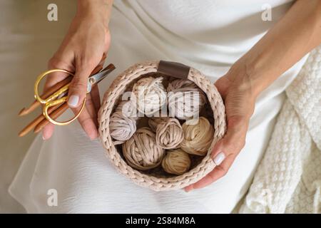Female hands holding a crocheted basket with skeins of cotton yarn in natural tones  Stock Photo