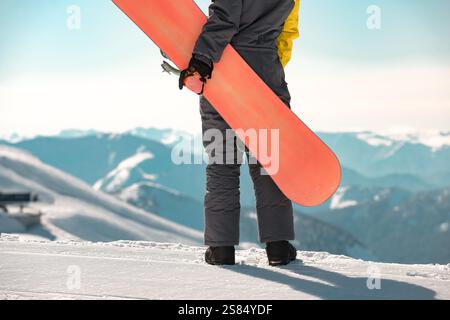 Girl snowboarder is standing with snowboard in hands at mountain top and looks at great view Stock Photo