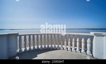 Marble terrace with ornate balusters framing serene lake waters, reflecting cloudless sky and radiating tranquil landscape atmosphere in Khabarovsk. Stock Photo