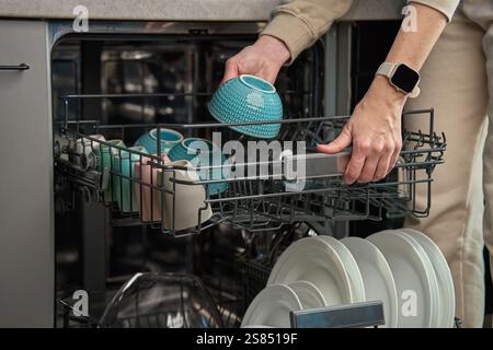 Woman unloading clean dishes and colorful bowl from dishwasher in kitchen. Person performing everyday household chores, using modern home appliance Stock Photo