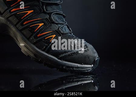 Close-up of waterproof black hiking boot with orange accents and water droplets. Rugged trekking shoe on dark background. Footwear for exploration and Stock Photo
