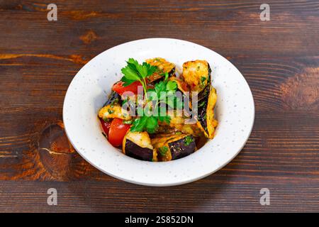 A delicious dish featuring grilled eggplant, tomatoes, and herbs arranged beautifully in a white bowl. Perfectly cooked and seasoned, served on a rust Stock Photo