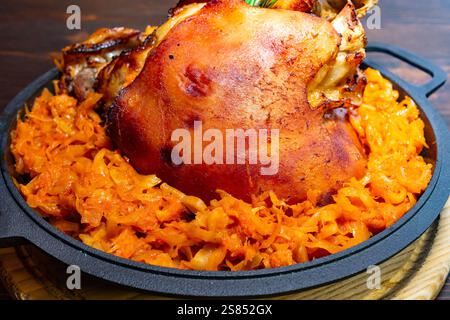 A succulent roasted pork knuckle rests on a bed of vibrant sauerkraut, showcasing a crispy, golden skin. The dish is presented on a rustic cast iron p Stock Photo