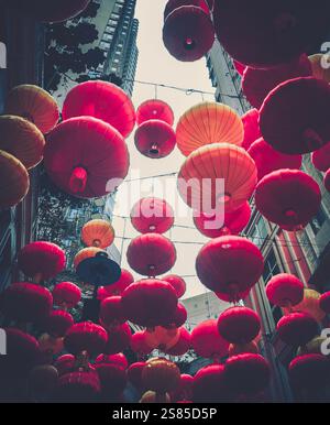 Vibrant red and orange lanterns hang densely between tall buildings, a festive display celebrating Chinese New Year.  The low angle shot emphasizes th Stock Photo