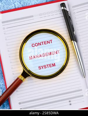A magnifying glass emphasizes the text CONTENT MANAGEMENT SYSTEM written in a notebook, illustrating key business technology concepts. Stock Photo