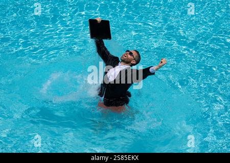 Funny business man in business suit with laptop jumping in splash water in the pool. Remote work. Crazy freelancer. Business and summer. Summer Stock Photo
