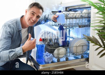 Smiling person showing dishwasher cleaning products next to a dishwasher full of clean dishes. Stock Photo
