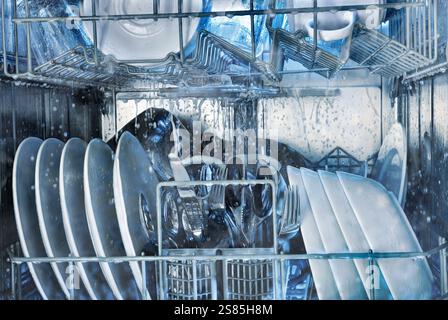 Details of the interior of a running dishwasher washing tableware with grey and blue tones. Front view. Stock Photo